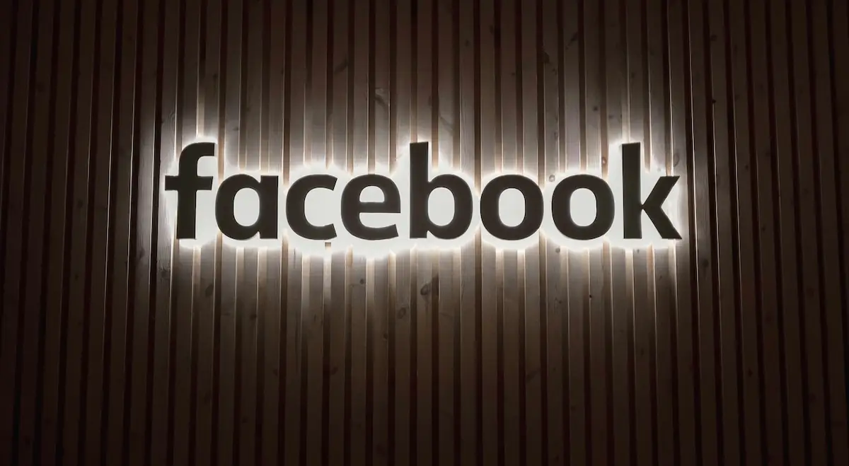 Leuchtender Facebook-Schriftzug auf Holzwand – Symbol für digitale Präsenz im Social Web